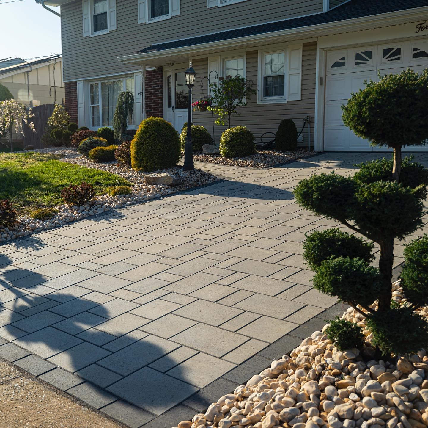 Paver driveway walkway with topiaries and river rock borders