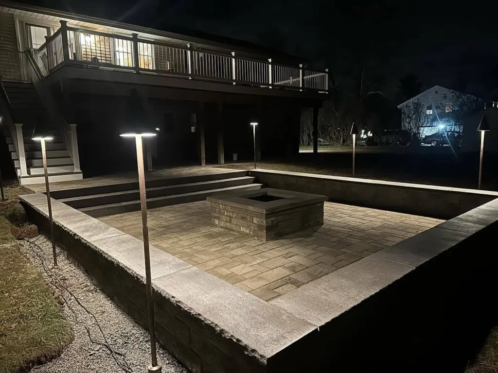 Side view of a newly installed Techobloc outdoor living area with a fire pit and outdoor night time lighting
